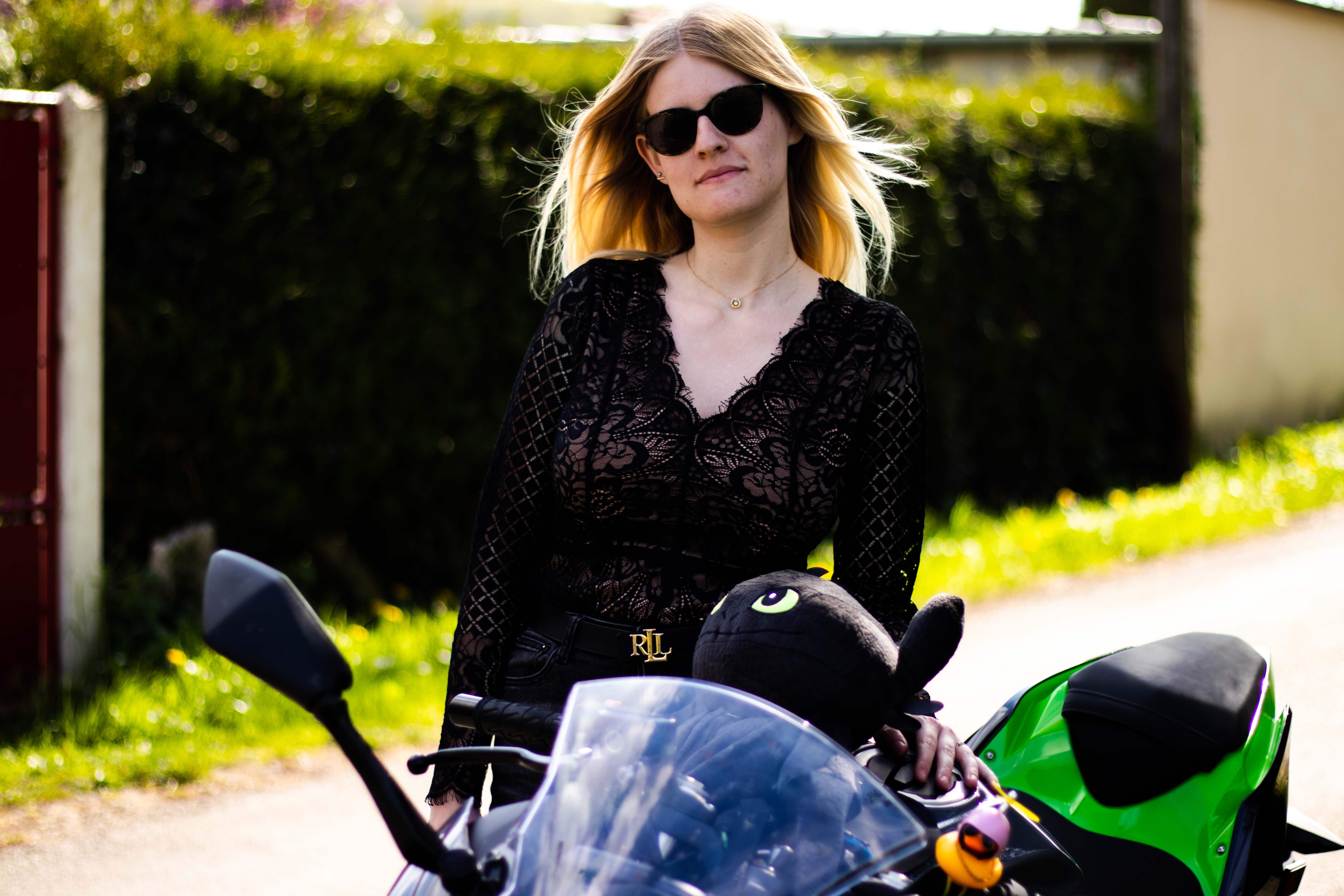 Photo d'une femmme avec des lunettes de soleil s'appuyant contre une moto avec la main gauche ayant les cheveux se soulevant avec le vent